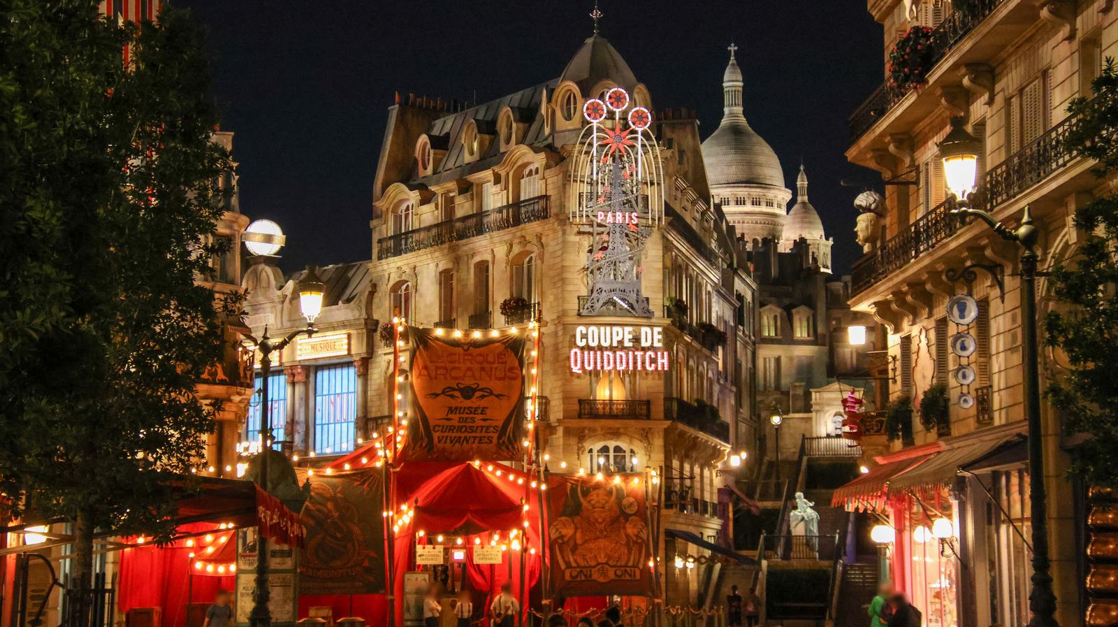 The Paris street of the Ministry of Magic land at Epic Universe at night, with Le Cirque Arcanus and the Coupe de Quidditch sign